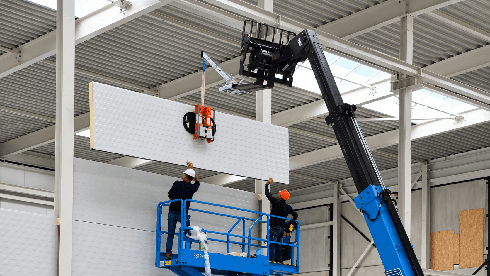 Trabajadores instalando panel metálico aislante con ventosa VIAVAC y grúa en nave industrial